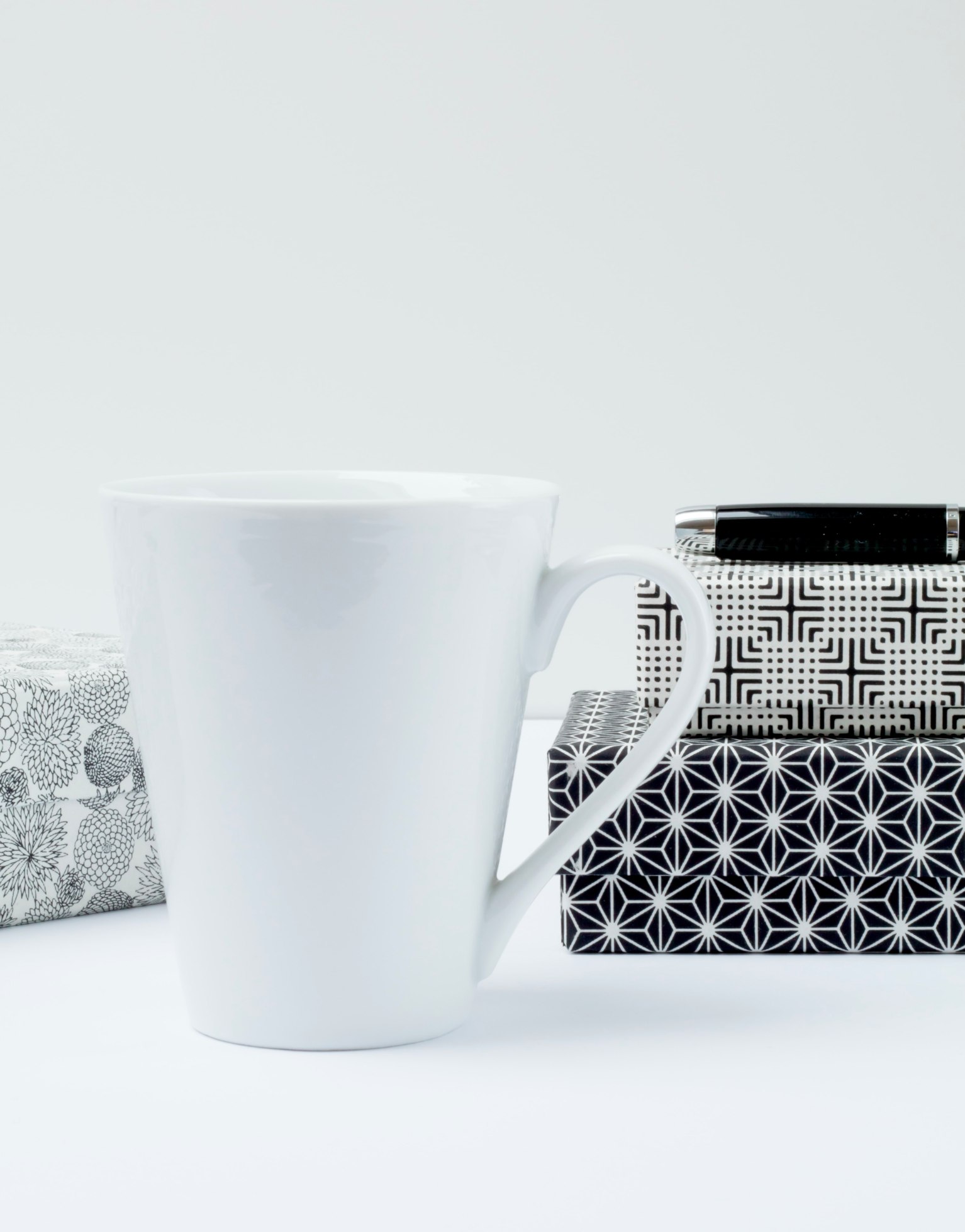 White mug in front of books and pen